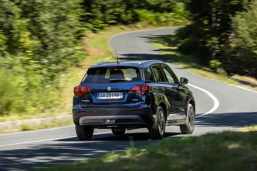 Suzuki Vitara 2023 roulant sur une route sinueuse en pleine nature.