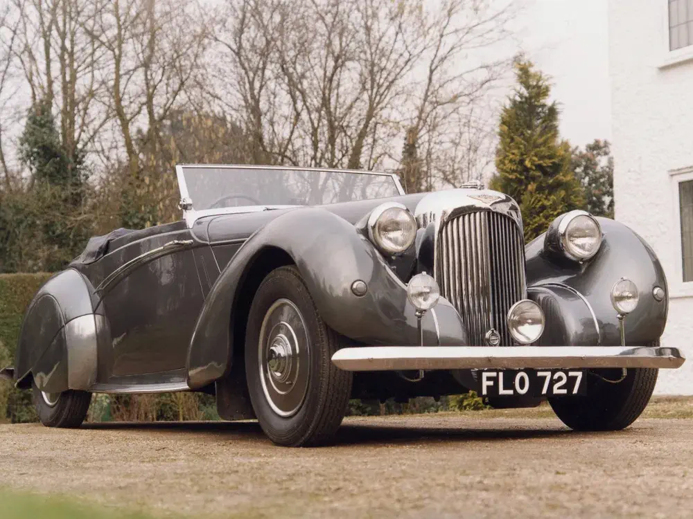 Voiture classique bicolore, décapotable avec plaque FLO 727, stationnée sur allée pavée.