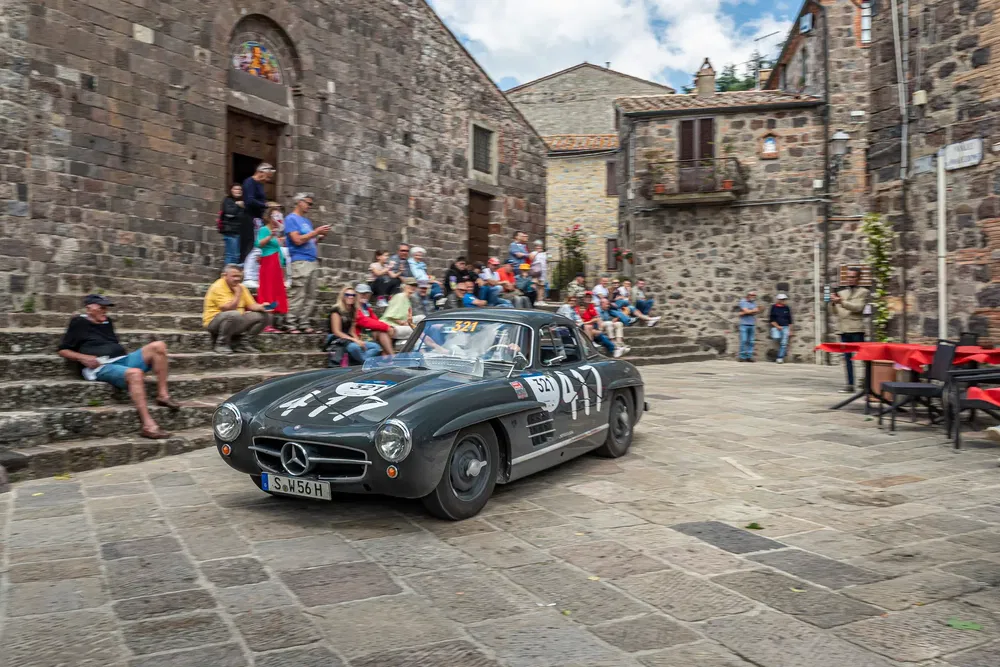 Mercedes-Benz 300 SL classique sur une place pavée, entourée de spectateurs admiratifs.