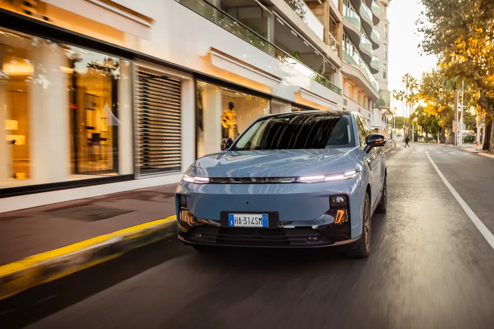 Voiture électrique moderne sur route urbaine bordée de boutiques élégantes au crépuscule.