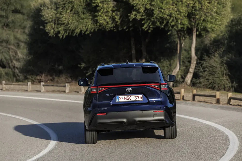 Achteraanzicht van een zwarte Toyota bZ4X op een bochtige weg omgeven door bomen.