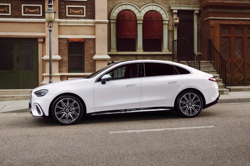 Mercedes-Benz EQE blanc stationné dans une rue urbaine devant des bâtiments en briques.