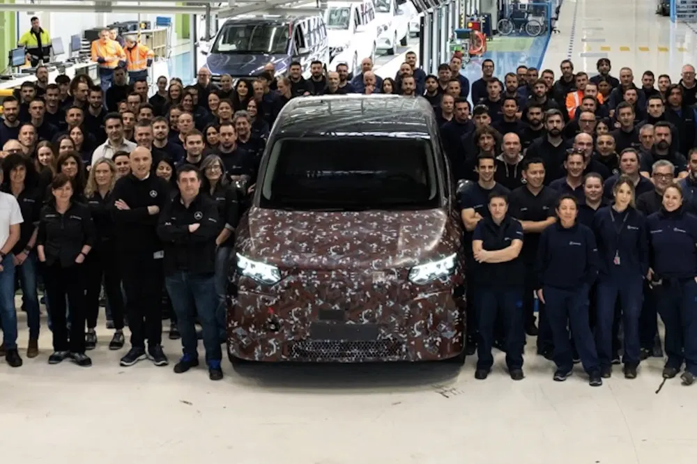 Fabrieksmedewerkers rond een gecamoufleerd Mercedes-Benz voertuig op een autoproductielijn.