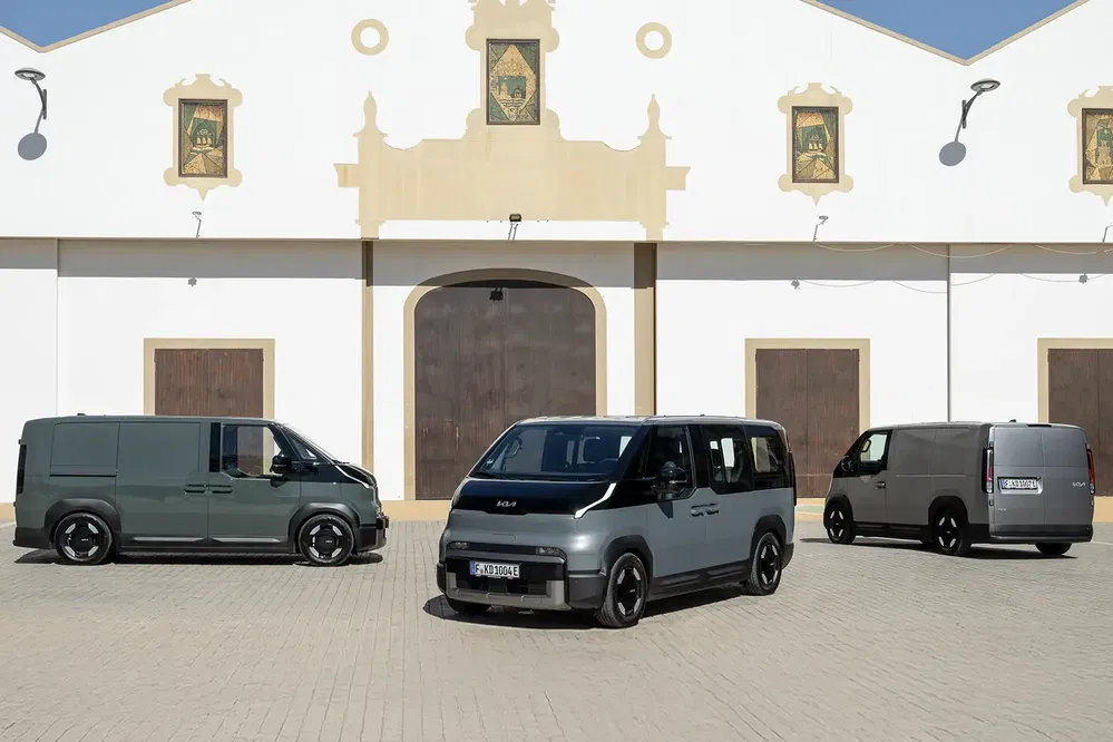 Trois fourgons Kia électriques garés devant un bâtiment historique.