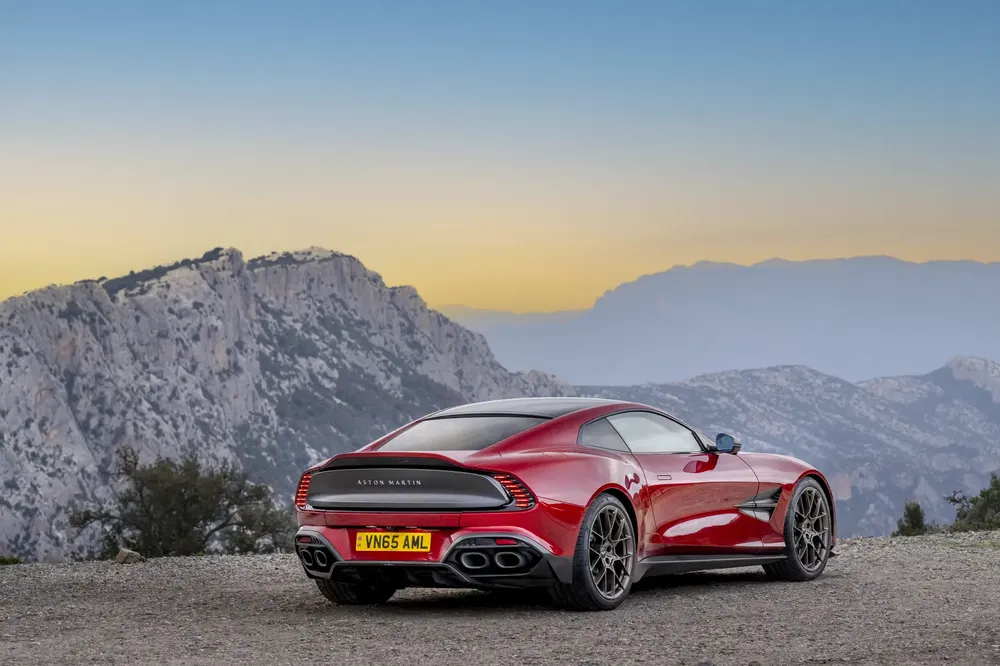 Aston Martin rouge devant un paysage montagneux, au coucher du soleil.