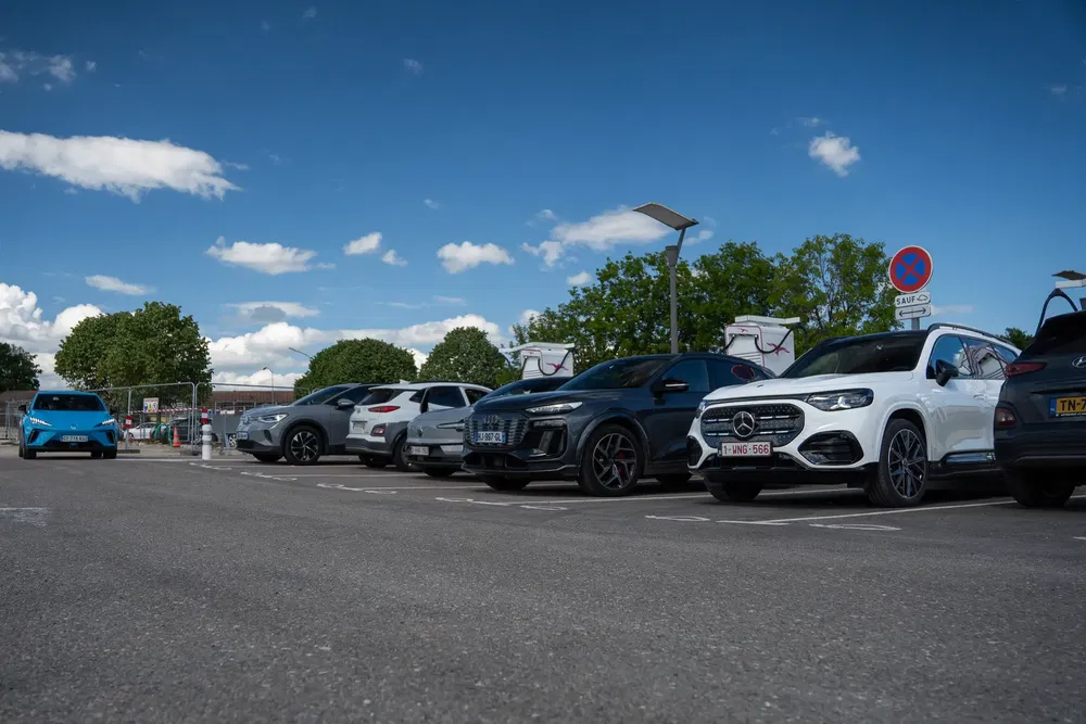 Parking avec SUV Mercedes blanc et voitures électriques sous ciel dégagé.