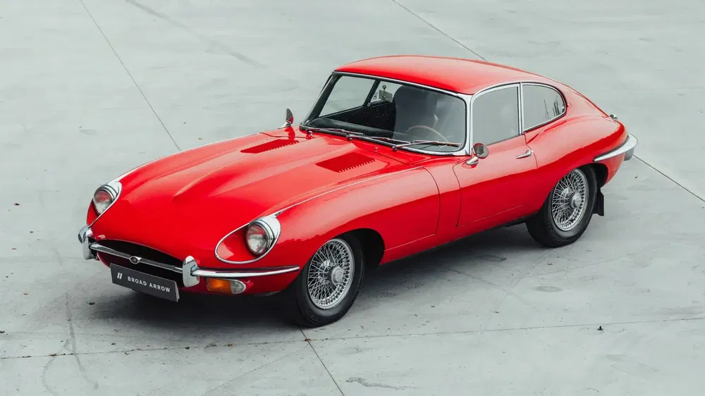 Jaguar E-Type rouge classique garée, design élégant et iconique des années 60 sur fonds urbains.