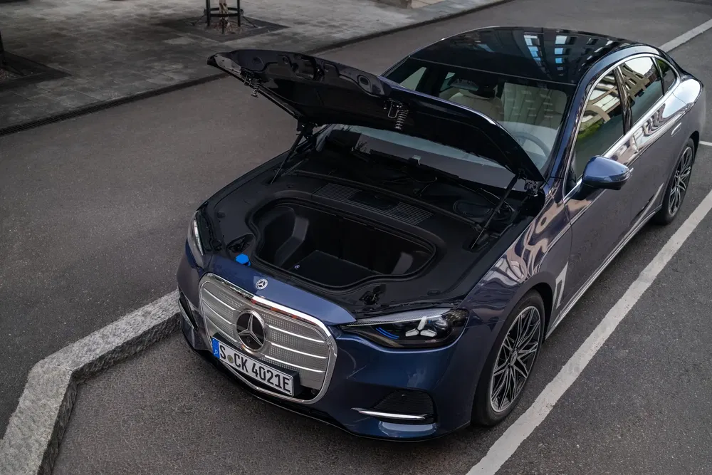 Mercedes électrique avec capot ouvert révélant le rangement avant, stationnée sur une rue.