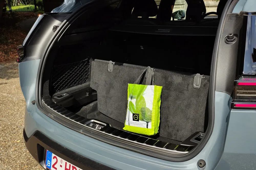 Coffre d'une voiture électrique avec sac de courses vert, plaque belge visible.