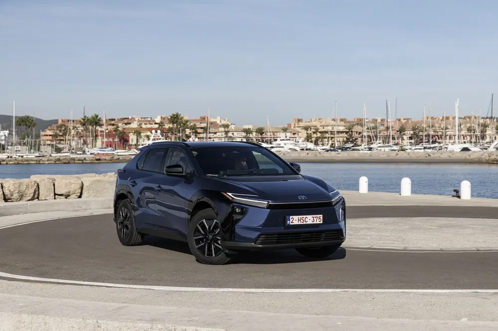 Zwarte Toyota bZ4X SUV geparkeerd bij haven, heldere hemel, uitzicht op jachten.