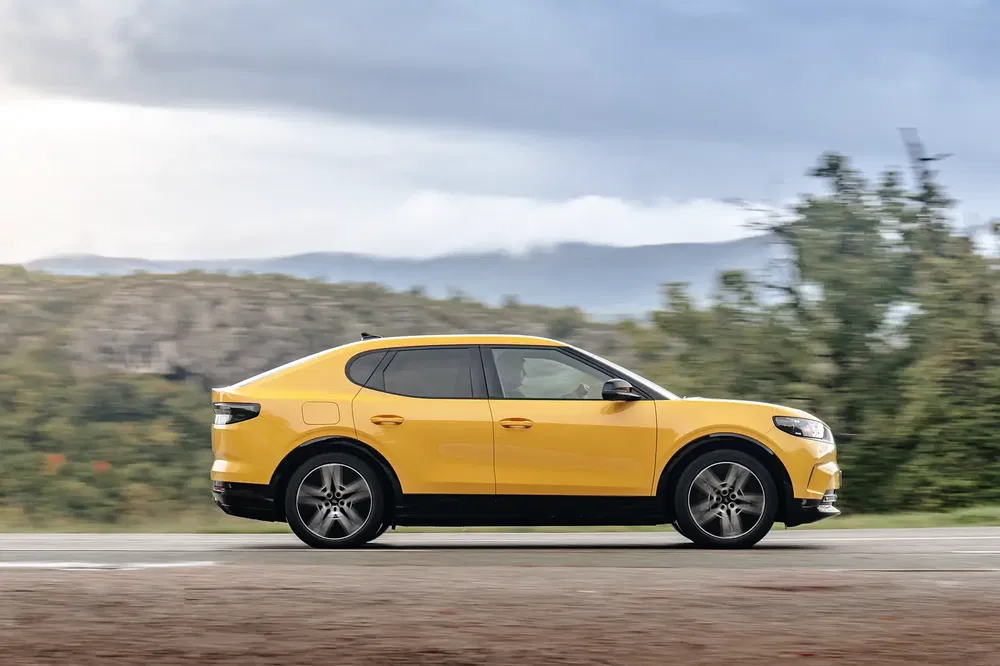 Voiture électrique MG4 jaune roulant sur route, paysage de campagne en arrière-plan.