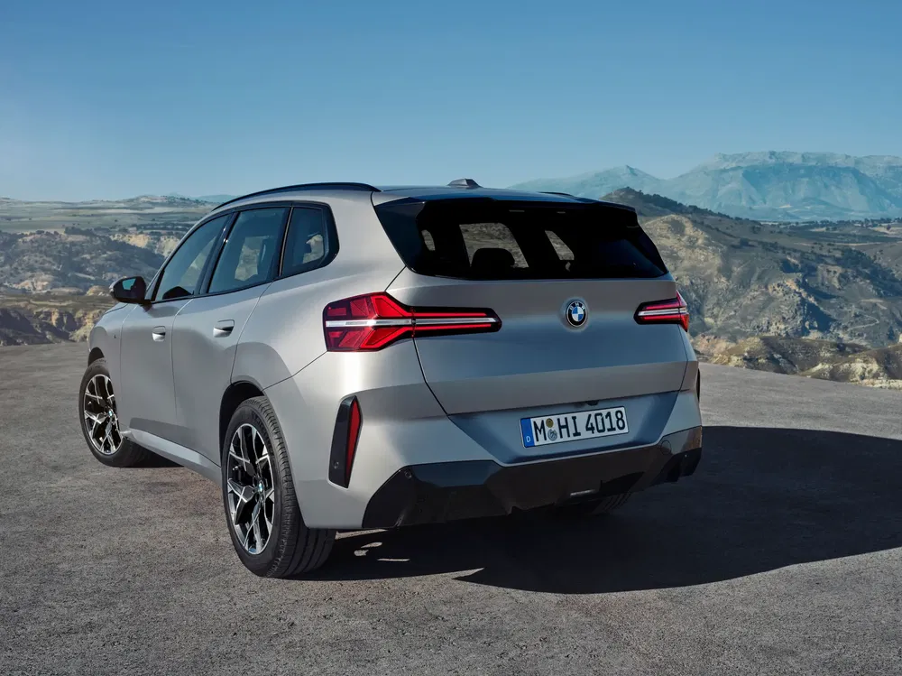 BMW X3, vue arrière sur route montagneuse avec feux arrière allumés.
