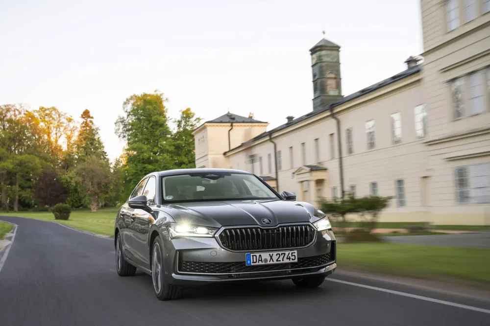 Škoda berline grise roulant devant un bâtiment historique, sur une route bordée d'arbres.