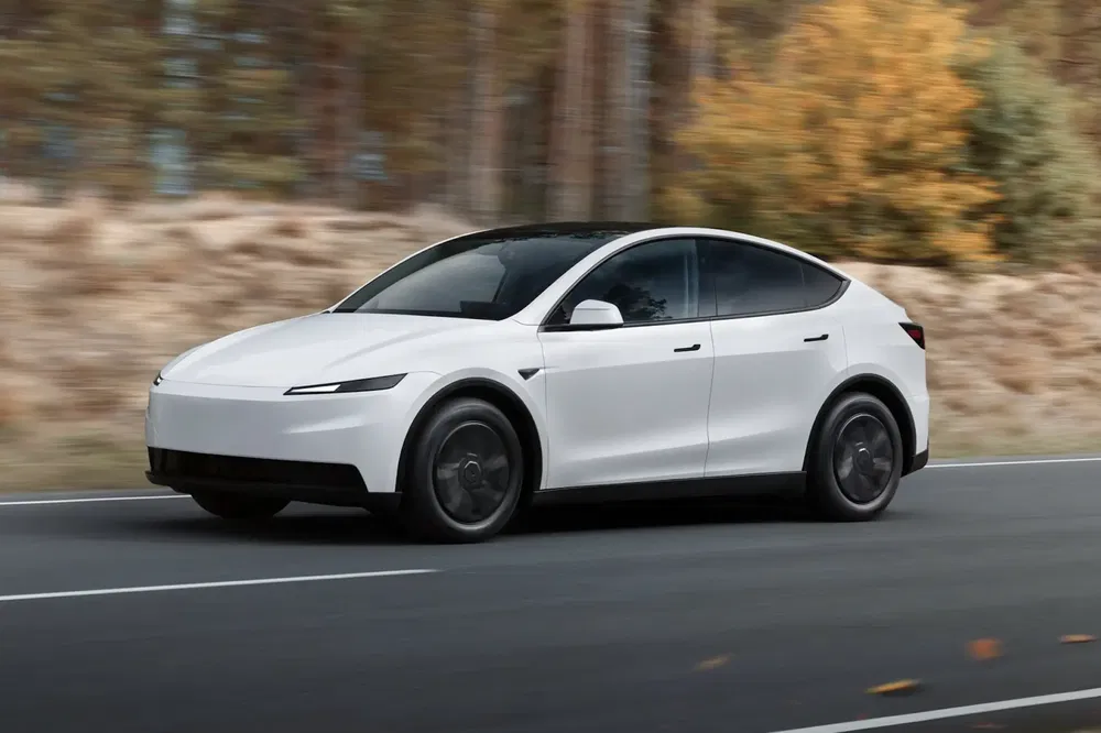 Witte Tesla Model Y rijdt op weg omringd door herfstbomen.