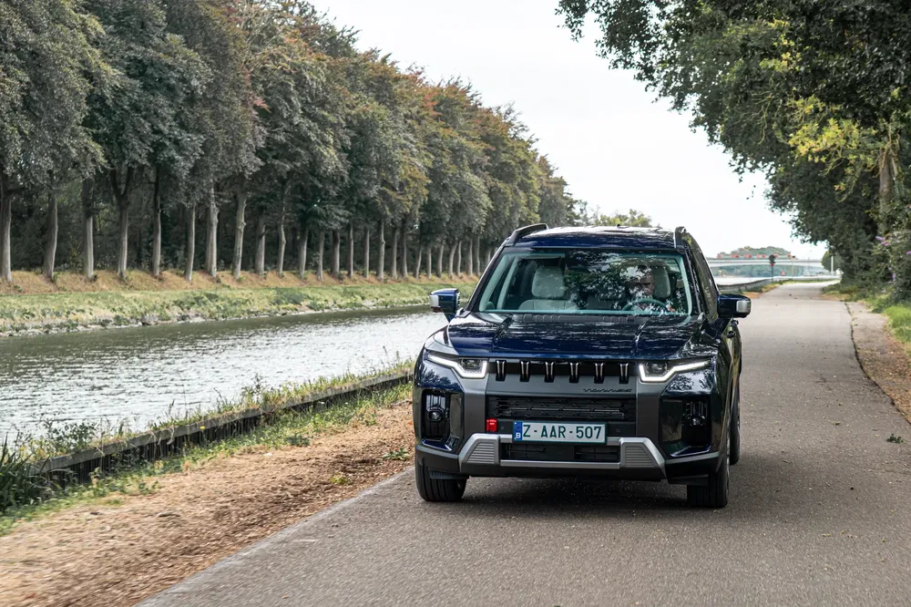 SUV Mitsubishi sur route de campagne bordée d'arbres, près d'un canal pittoresque.