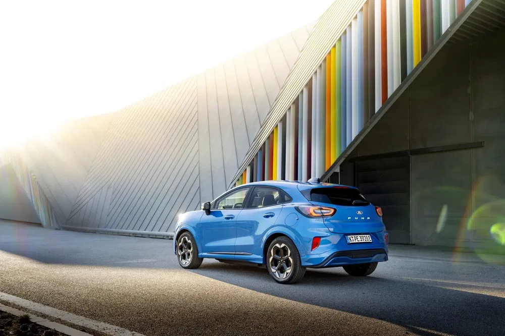 Ford Puma bleu stationné devant un bâtiment moderne et coloré au lever du soleil.