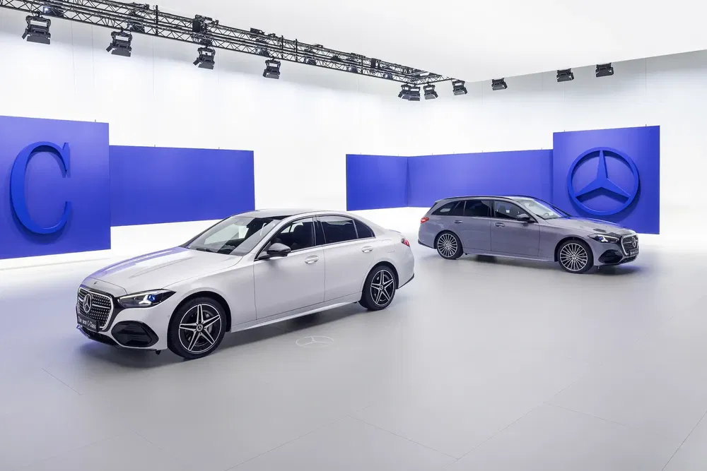 Deux Mercedes-Benz Classe C exposées dans une salle moderne avec logo en arrière-plan.