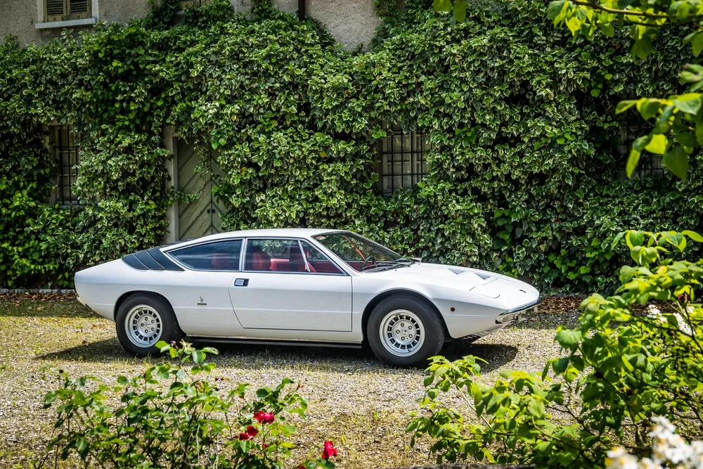 Witte Ferrari Dino 308 GT4 geparkeerd voor een groene klimopmuur.