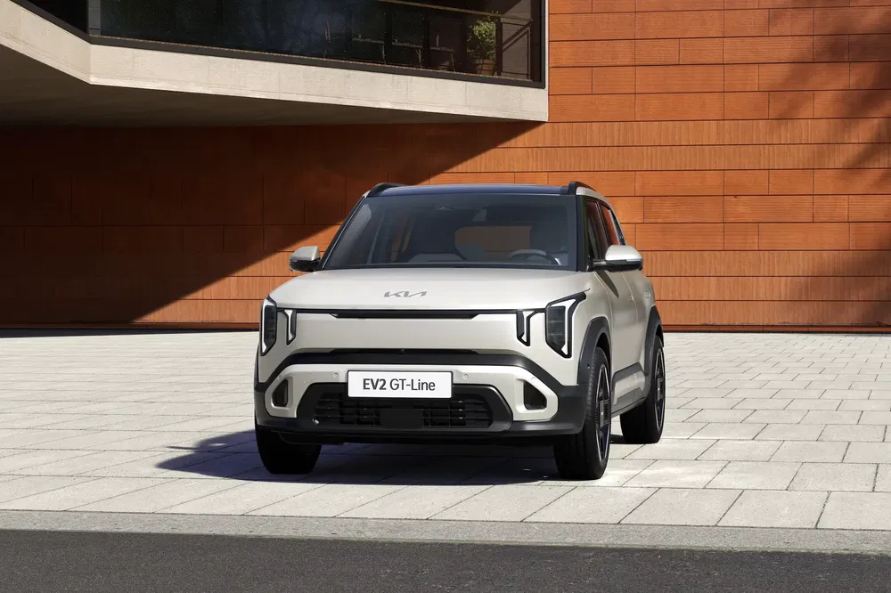 Zilveren Kia EV2 GT-Line geparkeerd voor een modern rood bakstenen gebouw.