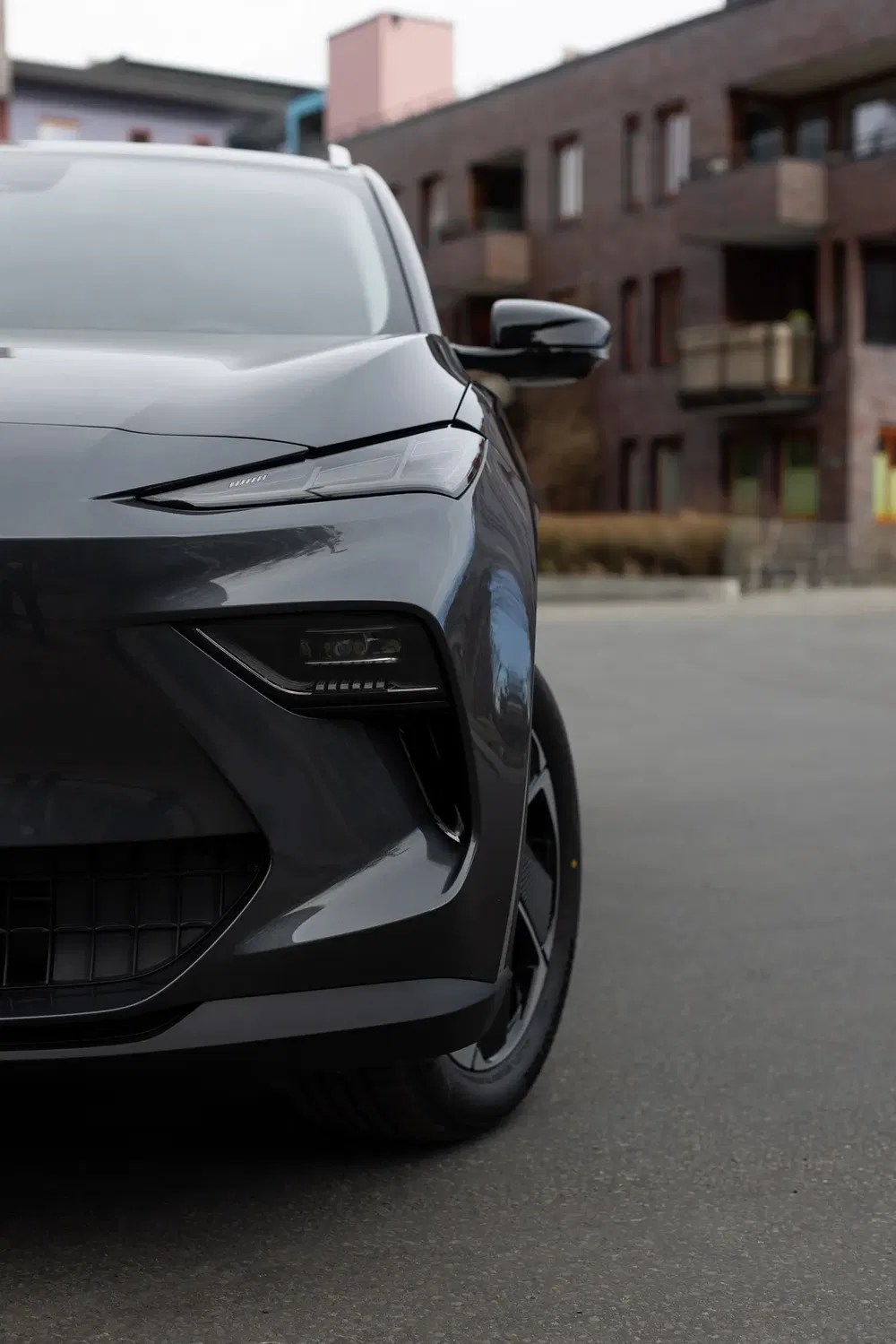Demi avant de voiture électrique sombre, design moderne, devant bâtiments résidentiels.