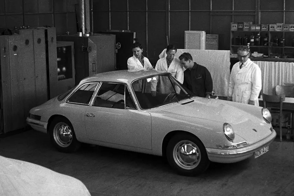 Prototypische Porsche 911 in fabriek met ingenieurs in discussie.