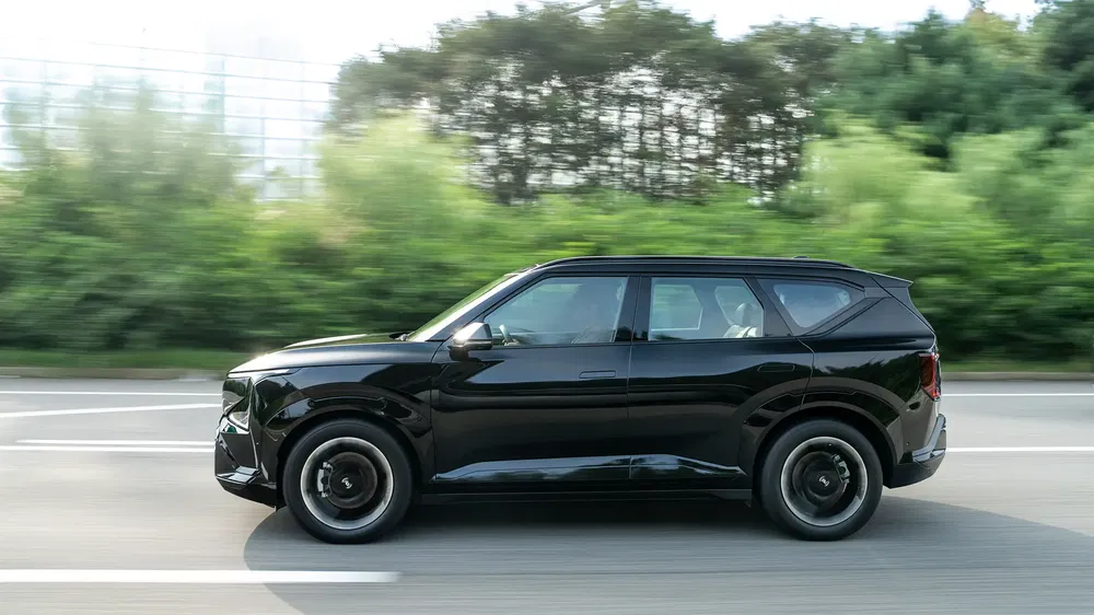 SUV noir en mouvement sur l'autoroute, entouré de verdure, vue latérale.