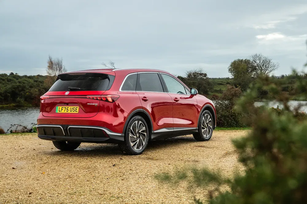 Rode MG SUV geparkeerd op onverharde weg met rivier en vegetatie op de achtergrond.