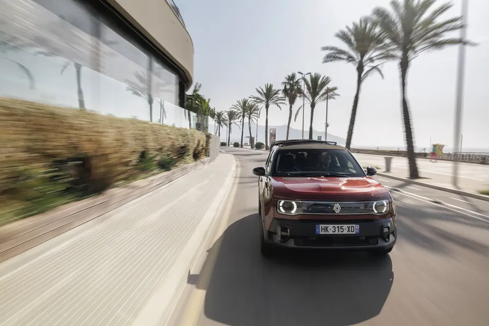 Renault red SUV on coastal road flanked by palm trees, showcasing dynamic urban driving.