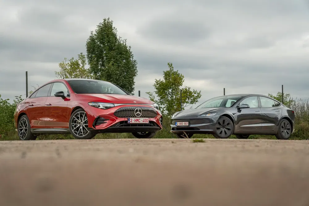 Mercedes rouge et Tesla grise côte à côte sous un ciel nuageux.