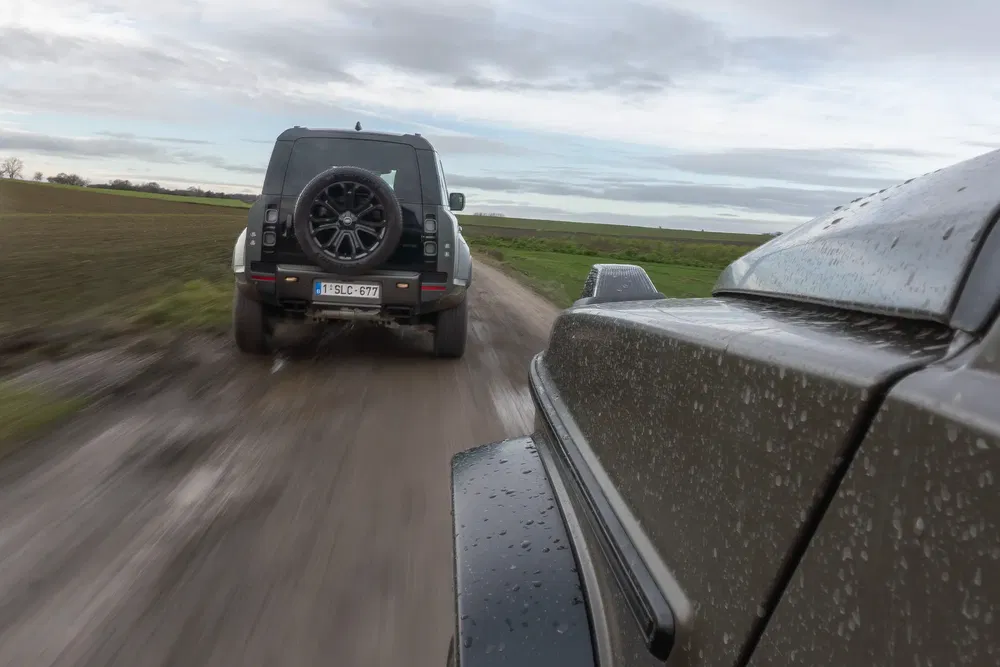Deux SUV Land Rover Defender sur une route boueuse, roulant à haute vitesse.