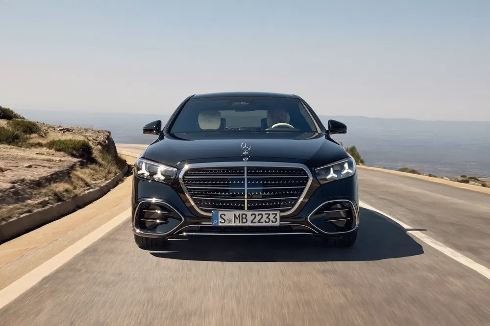 Zwarte Mercedes-Benz S-Klasse rijdt op kustweg, dynamisch vooraanzicht.