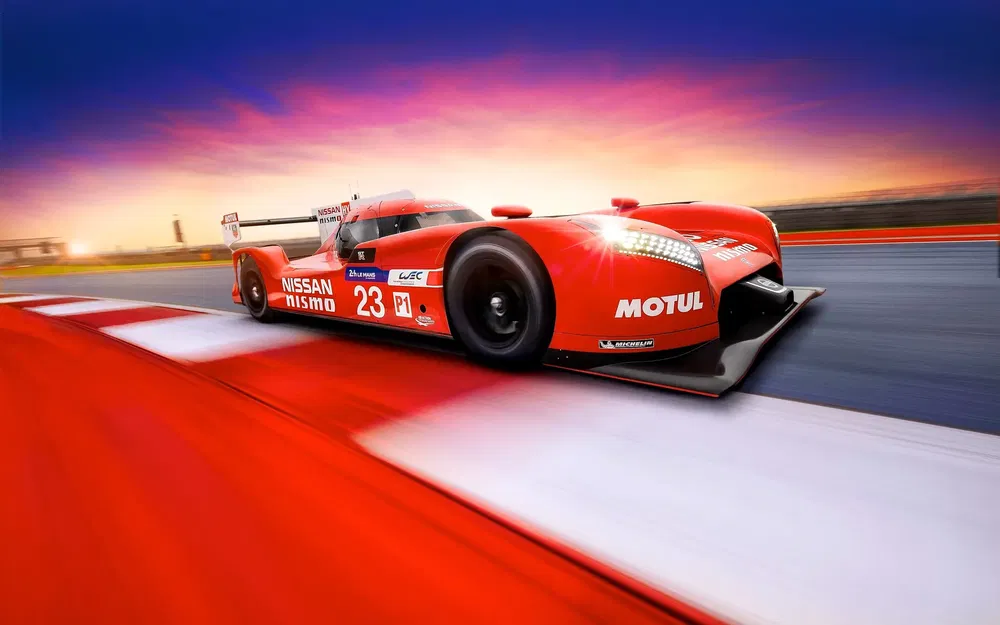 Voiture de course Nissan Nismo rouge sur piste au coucher du soleil, numéro 23 visible.