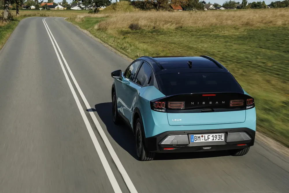 Blauwe Nissan Leaf op landelijke weg, moderne elektrische auto in beweging.