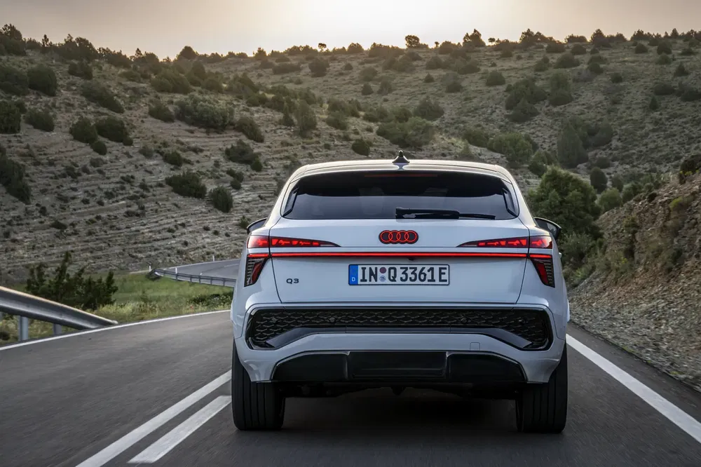 Vue arrière de l'Audi Q3 blanche sur route de montagne au crépuscule.