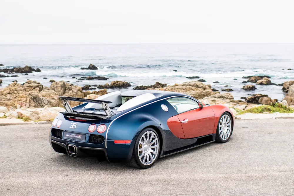 Bugatti Veyron bleu et rouge stationnée sur une côte rocheuse avec vue sur l'océan.