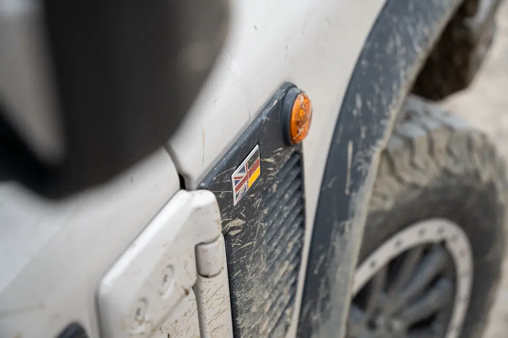 Detail van een modderige Land Rover Defender met Union Jack-sticker.