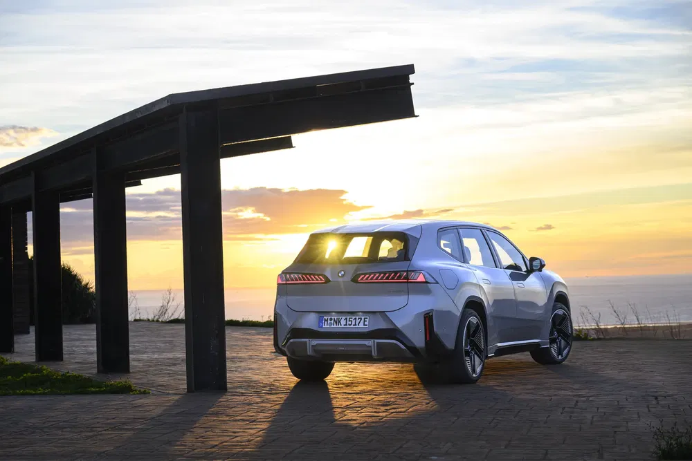 SUV BMW blanc garé au coucher du soleil près d'un abri moderne.