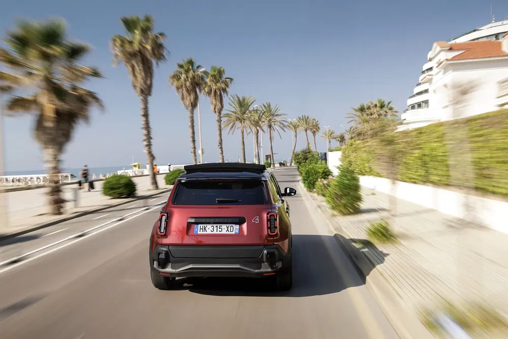 Mini Cooper Countryman roulant sur une route côtière bordée de palmiers.