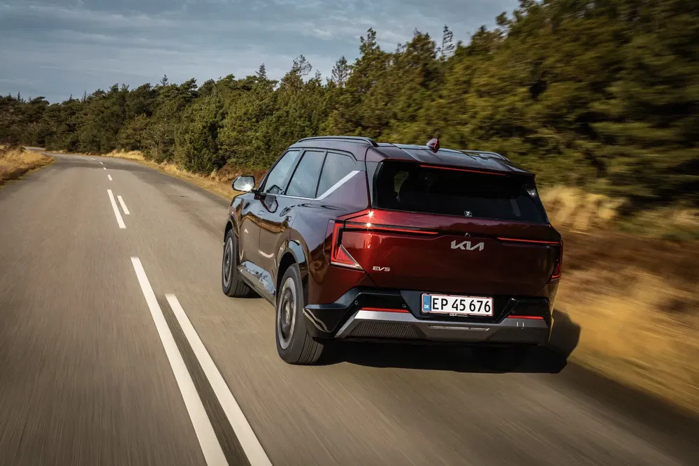 SUV Kia EV5 rouge sur une route de campagne bordée d'arbres.