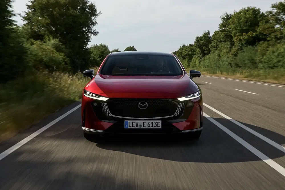 Mazda CX-60 rouge roulant sur une route bordée d'arbres, avant imposant.