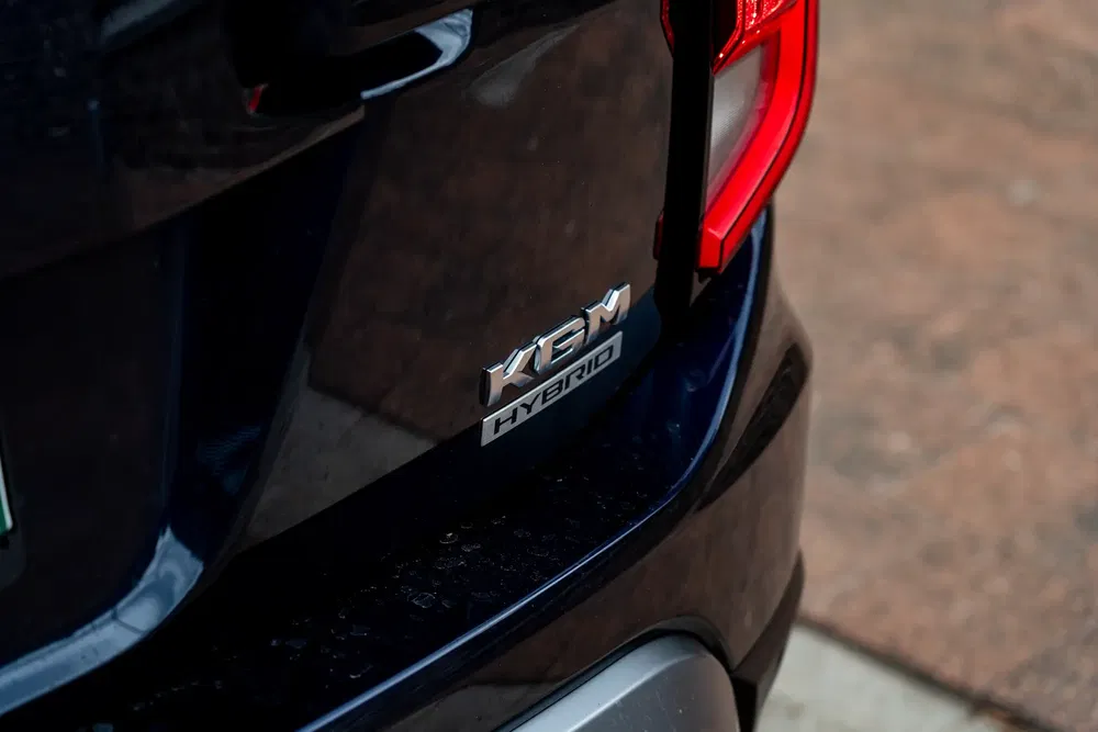 Emblème Kia hybride sur coffre arrière avec carrosserie bleu foncé.