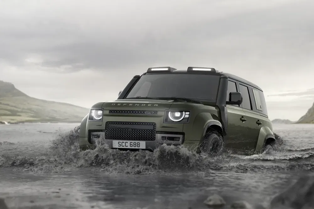 Land Rover Defender traversant une rivière dans un paysage montagneux, démontrant sa capacité tout-terrain.