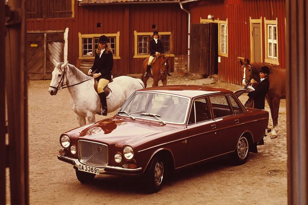 Rode vintage Volvo geparkeerd voor een stal met ruiters te paard.