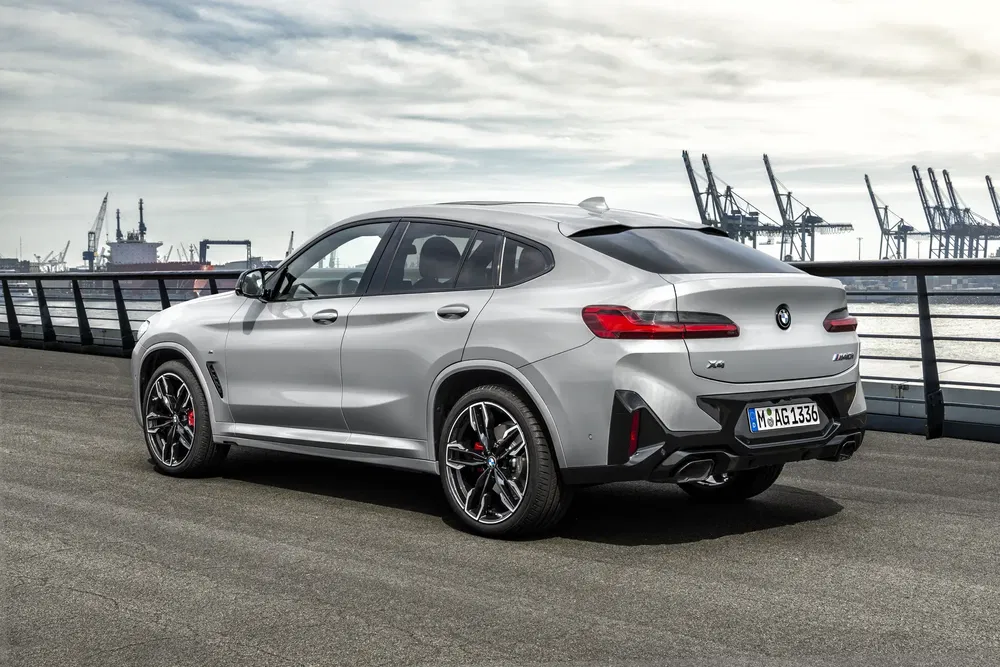 Zilveren BMW X4 geparkeerd bij een industriële haven onder bewolkte hemel.