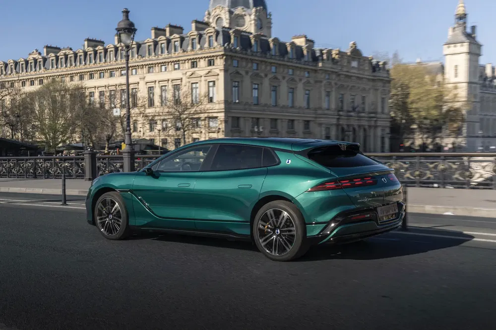 Peugeot 408 vert intense sur un pont parisien historique avec bâtiments emblématiques en arrière-plan.