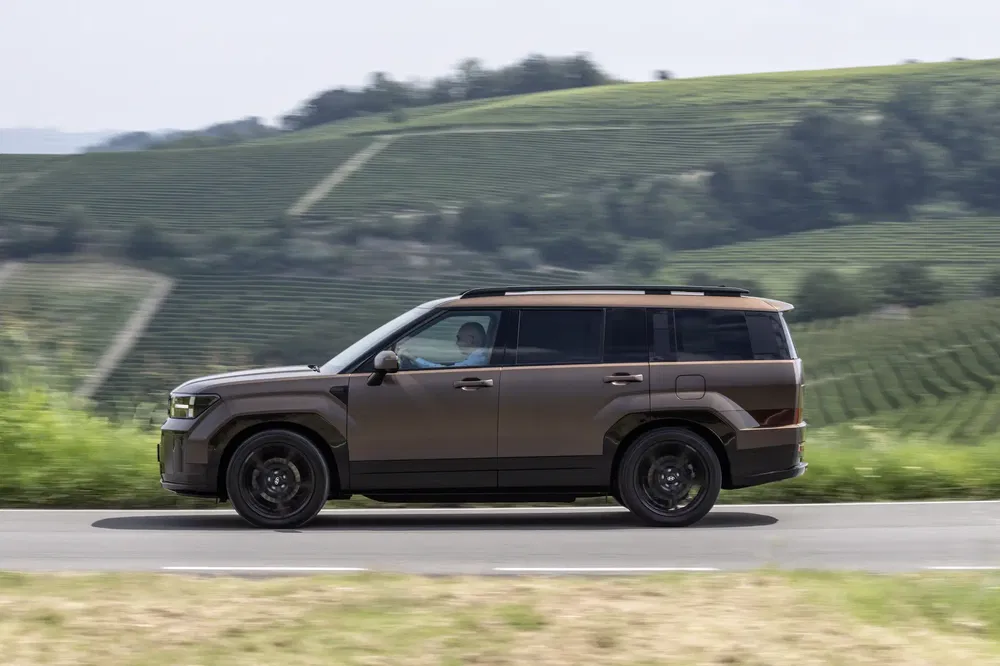 Moderne elektrische SUV op plattelandsweg met heuvels op de achtergrond.