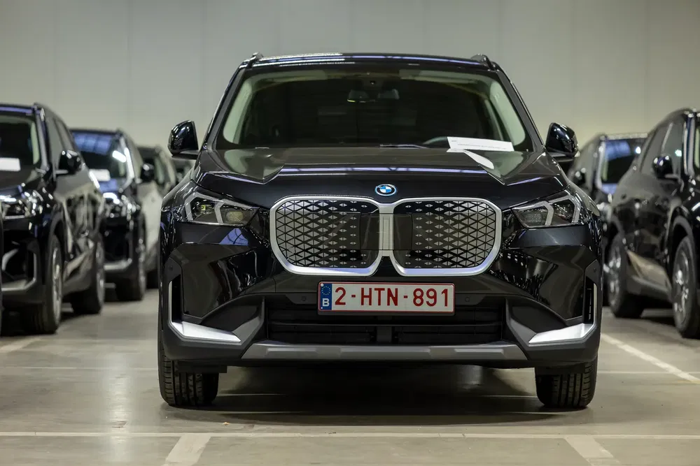 BMW iX électrique garée dans un garage avec plaque d'immatriculation belge visible.