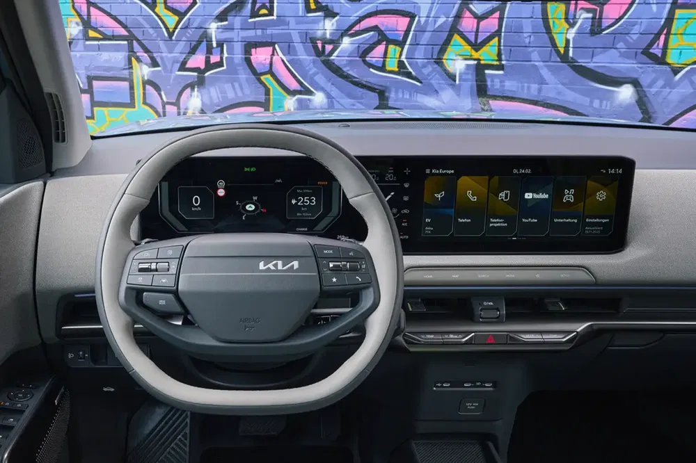 Intérieur de la Kia, volant et tableau numérique avec mur de graffiti à l'arrière-plan.