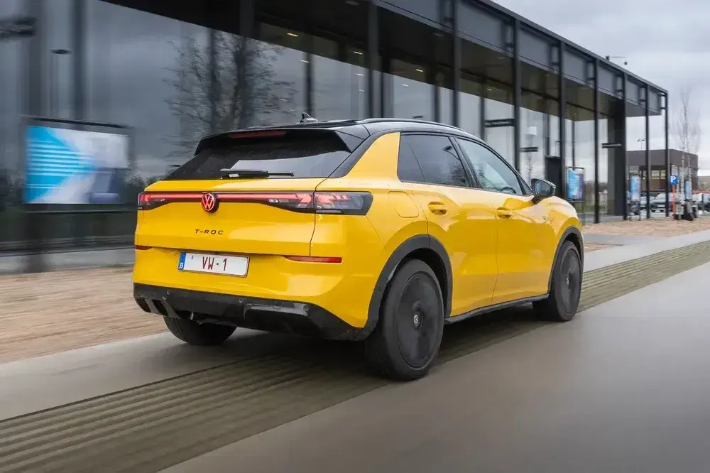 Volkswagen T-Roc jaune vif sur route près d'un bâtiment moderne, design arrière élégant.