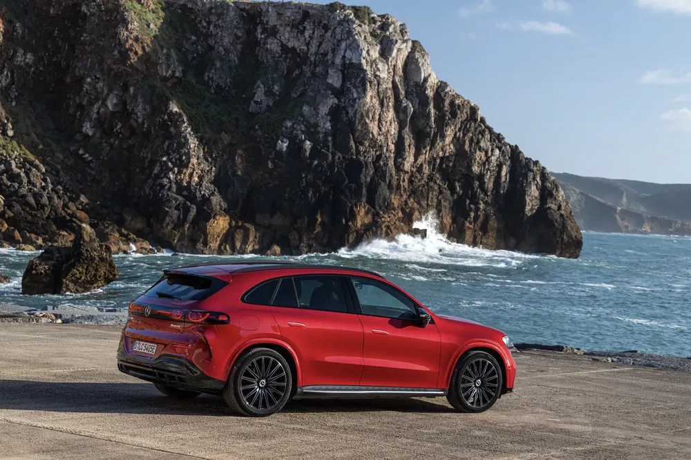 Rode Mercedes-Benz GLC geparkeerd voor rotsachtige klif met uitzicht op de oceaan.